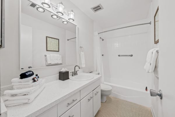 This image shows a clean, white bathroom with a bathtub, sink, mirror, and countertop. Towels are neatly folded on the counter and a towel bar.