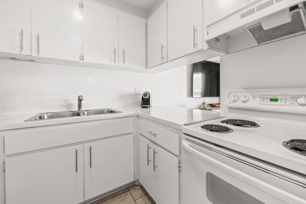 A modern white kitchen with cabinets, an electric stove, a sink, and a coffee maker on the counter, featuring a clean and minimalist design.