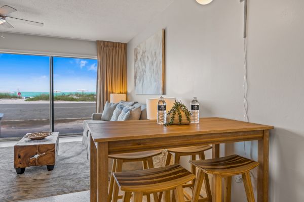 A cozy living area with a wooden dining table, stools, a couch, large window with an ocean view, and a coffee table.