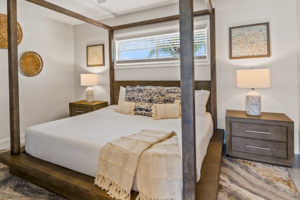 A cozy bedroom with a canopy bed, two bedside tables with lamps, wall art, and a decorative throw blanket is pictured.