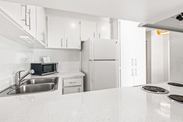 A modern white kitchen features a sink, stove, refrigerator, microwave, and ample cabinetry for storage.