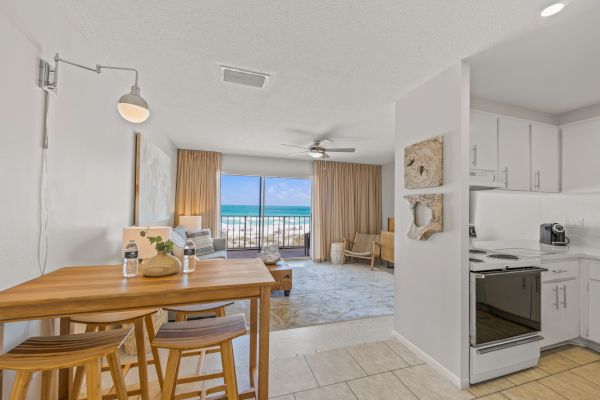 A modern beachfront studio apartment with a kitchen, dining area, and living space leading to a balcony showing the ocean view.