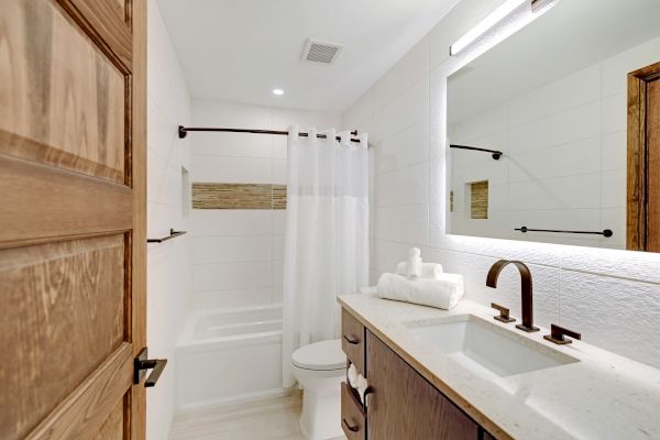 A modern bathroom featuring a wooden door, a vanity with a sink and mirror, a shower-tub combo with a white curtain, and neatly rolled towels.