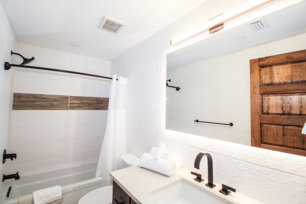 A modern bathroom with a bathtub, shower curtain, sink, large mirror, towels, and wooden door.