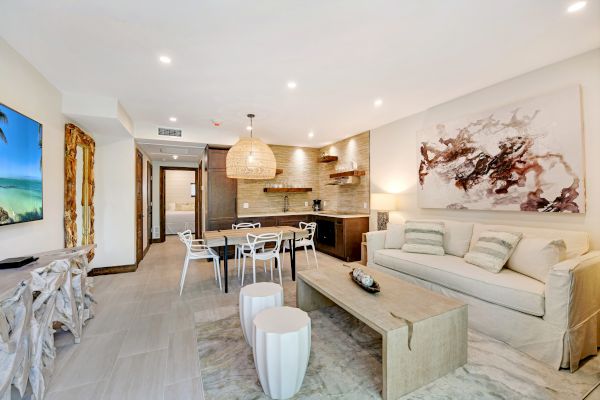 A modern living room and kitchen with neutral tones, art on the wall, TV, dining table, and a cozy seating area with a sofa and coffee table.