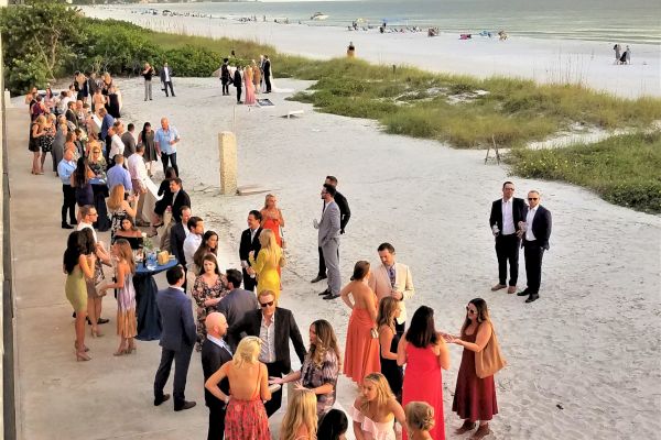 People in formal attire are gathered on a beachside promenade, mingling and enjoying what appears to be a social event or celebration.