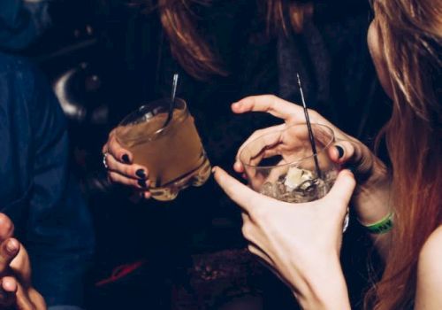 People socializing with drinks, hands raised in conversation, one person laughing, capturing a lively moment in a dim setting.