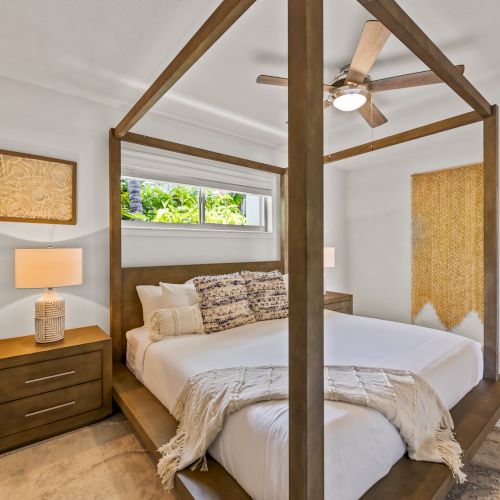 This image depicts a bedroom with a four-poster bed, two bedside tables with lamps, a ceiling fan, and a window with a nature view.