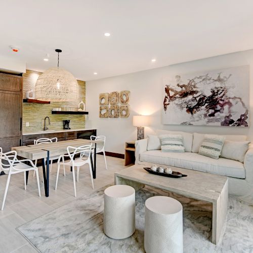 A modern living space with a dining area, kitchen, and sitting area. The decor is contemporary with light colors and artistic touches ending the sentence.