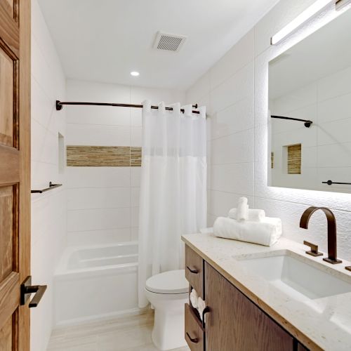 This image shows a modern bathroom with a shower and tub, a toilet, a sink with a countertop, and a large mirror, all in a clean, light design.