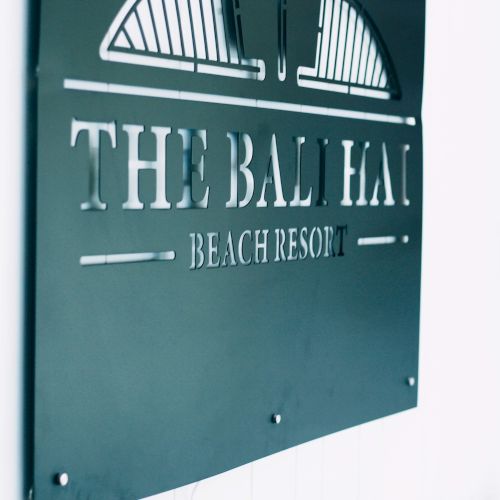 The image shows a sign that reads "The Bali Hai Beach Resort" mounted on a white wall with some wooden decoration on the side.